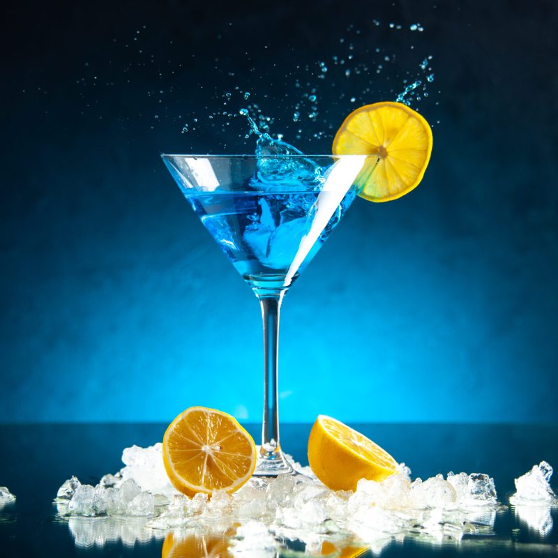 vista-superior-del-delicioso-coctel-en-una-copa-de-vidrio-servido-con-una-rodaja-de-limon-sobre-fondo-azul